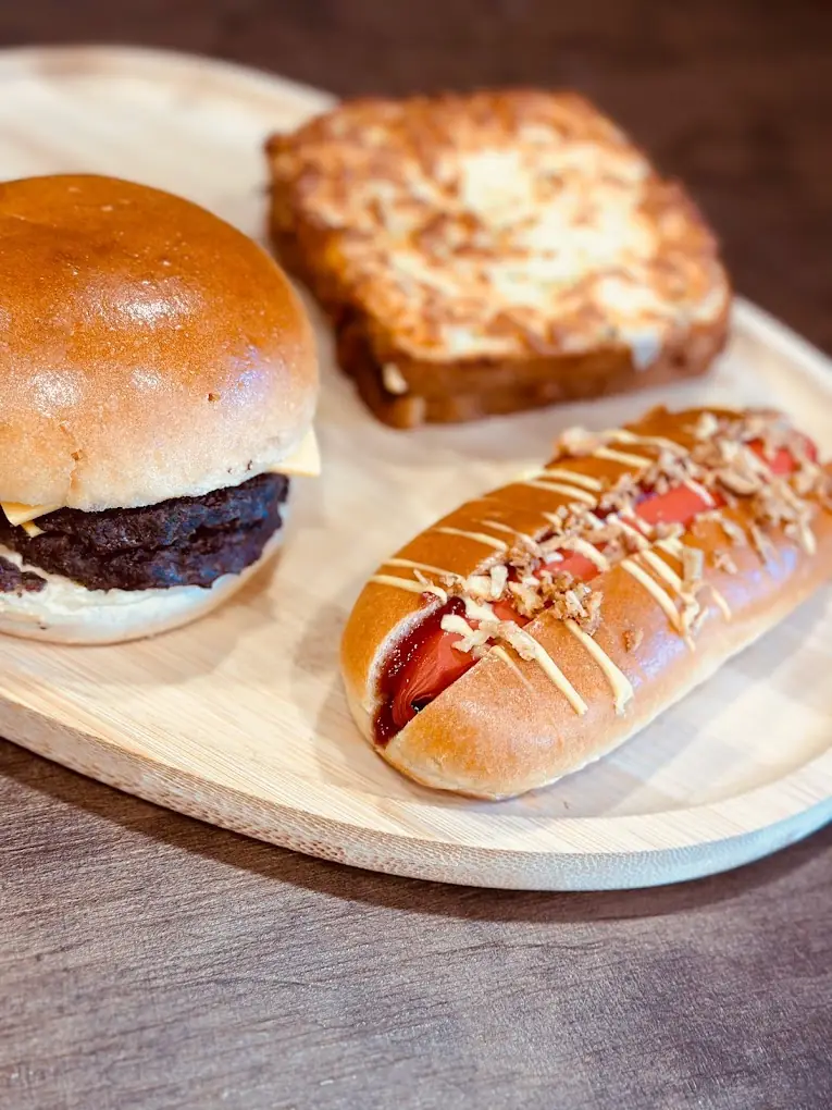 Un burger au fromage, un hot-dog aux oignons croustillants et un pain doré sur une planche en bois