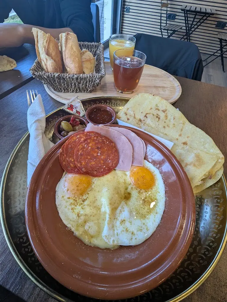 Le petit-déjeuner marocain : œufs au plat, tranches de charcuterie, olives, pain, msemen, jus d'orange et thé, servis sur un grand plateau